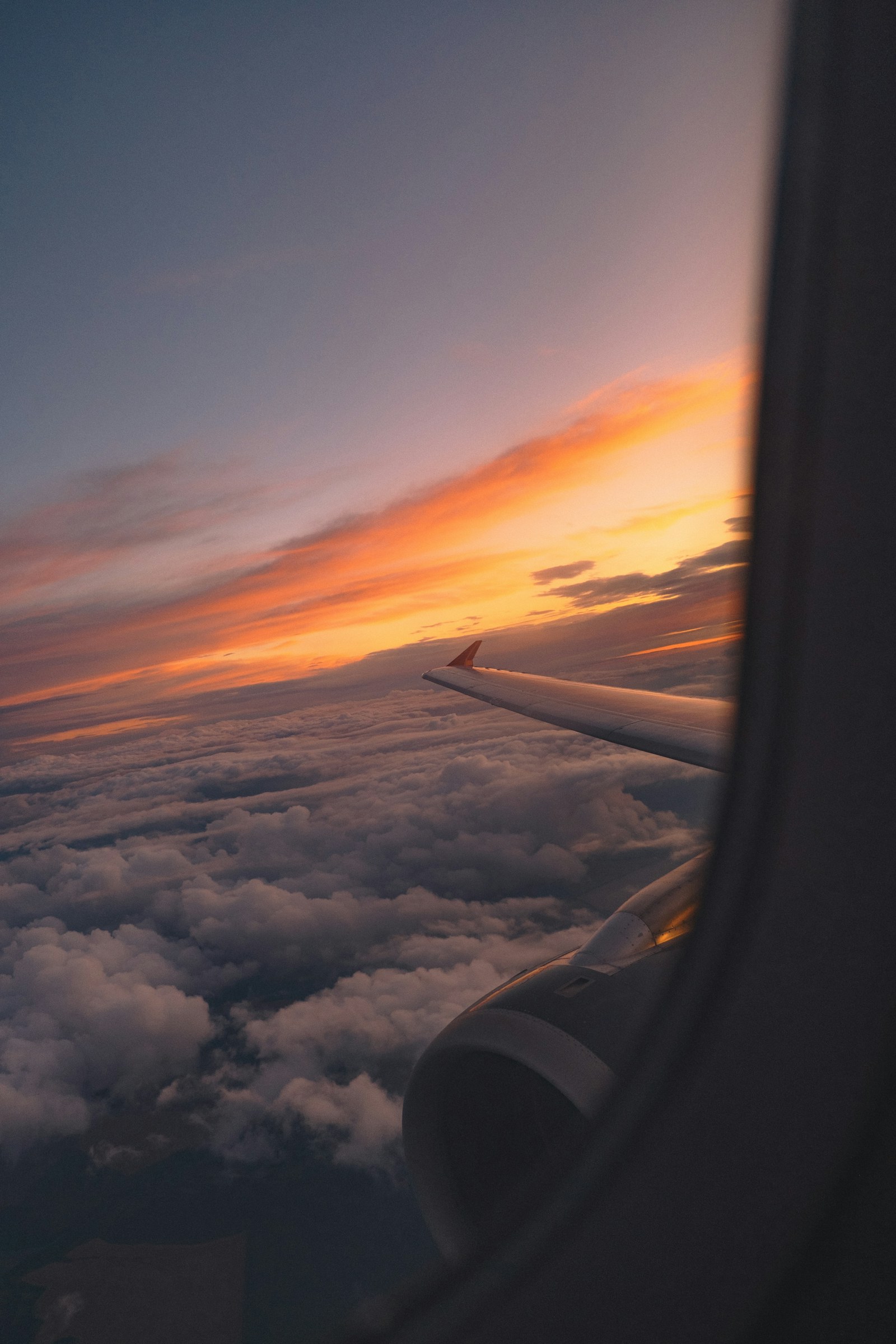 Airplane wing and engine flying above the clouds at sunset